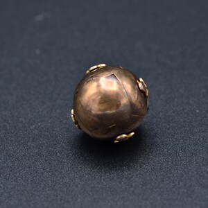 May include: A round, metallic, gold-colored bead with small, decorative, gold-colored accents.