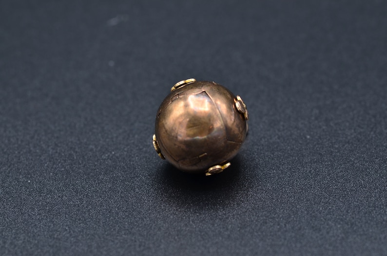 May include: A round, metallic, gold-colored bead with small, decorative, gold-colored accents.