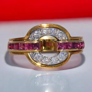 May include: A gold ring with a central oval design. The ring features a band of small, sparkling diamonds and a row of square-cut rubies. The ring has a polished gold finish and a bright, eye-catching appearance.