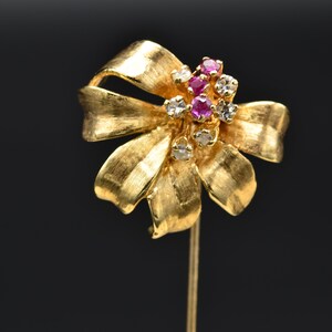 May include: A gold-toned brooch in the shape of a bow with red and clear rhinestones.