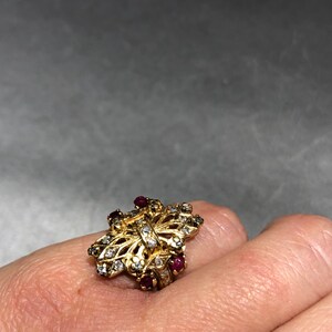 May include: A gold ring with a butterfly design set with small clear stones and red gemstones.