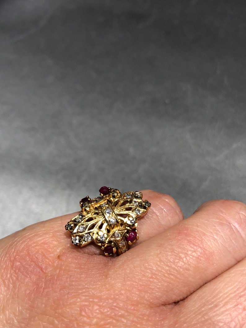 May include: A gold ring with a butterfly design set with small clear stones and red gemstones.