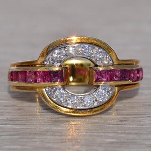 May include: A gold ring with a central circular design. The ring features a band of small, square-cut rubies and a section of white diamonds. The ring has a two-tone gold and silver appearance, with a polished finish.