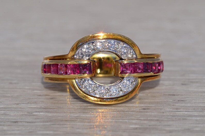 May include: A gold ring with a central circular design. The ring features a band of small, square-cut rubies and a section of white diamonds. The ring has a two-tone gold and silver appearance, with a polished finish.