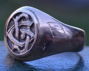 Puede incluir: Un anillo de plata con un diseño de monograma que presenta las letras "F" y "C" entrelazadas. El anillo tiene una banda lisa y un monograma en relieve en la cara.