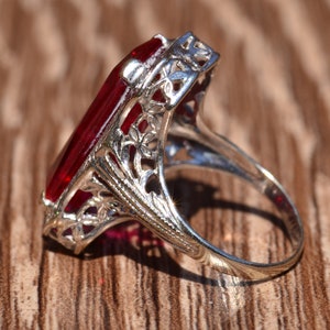 May include: A silver ring featuring a large, red, rectangular gemstone set in an elaborate filigree design.