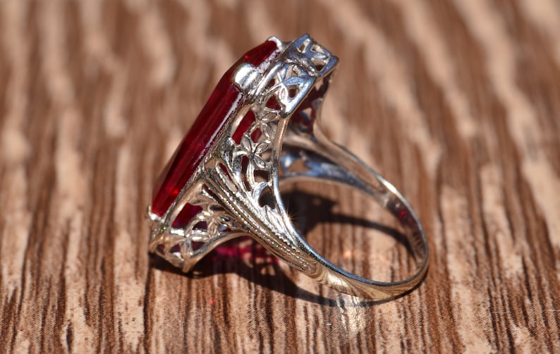 May include: A silver ring featuring a large, red, rectangular gemstone set in an elaborate filigree design.
