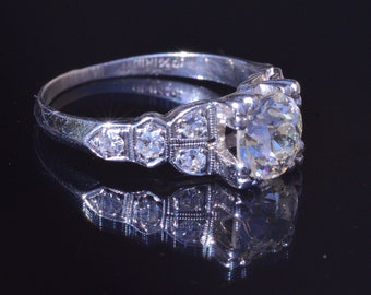 May include: A silver ring with a large round diamond in the center and smaller diamonds on the band.