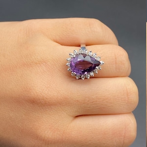 May include: A pear-shaped amethyst gemstone ring with a halo of smaller diamonds set in silver.