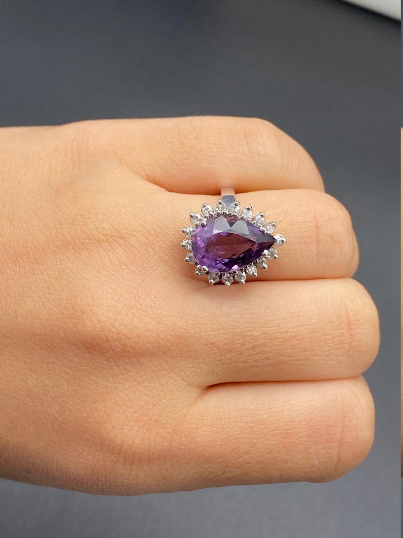 May include: A pear-shaped amethyst gemstone ring with a halo of smaller diamonds set in silver.
