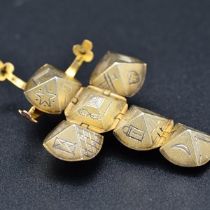 May include: A gold-colored, hinged, decorative object with a star, a pyramid, a lantern, and a crescent moon design. The object is made of metal and has a hinged design.