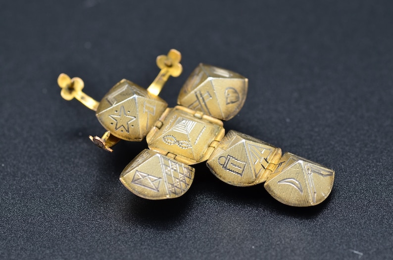 May include: A gold-colored, hinged, decorative object with a star, a pyramid, a lantern, and a crescent moon design. The object is made of metal and has a hinged design.