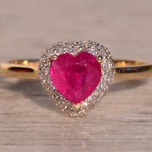 Könnte beinhalten: Ein Herz-förmiger Rubinring mit einem Halo aus kleineren Diamanten, gefasst in Gelbgold.