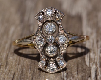 May include: A vintage diamond ring with a delicate, intricate design. The ring features a central cluster of three diamonds surrounded by smaller diamonds, set in a silver and gold band.