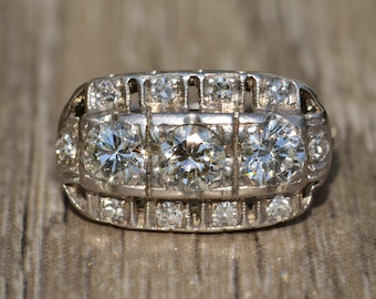 May include: A silver ring with a row of three large diamonds surrounded by smaller diamonds.