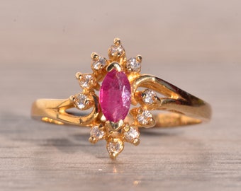 Op de afbeelding: Een gouden ring met een marquise-geslepen robijn als middensteen, omringd door kleine, ronde diamanten. De ring heeft een sierlijk, vloeiend ontwerp. De edelstenen zijn gezet in een gouden zetting.