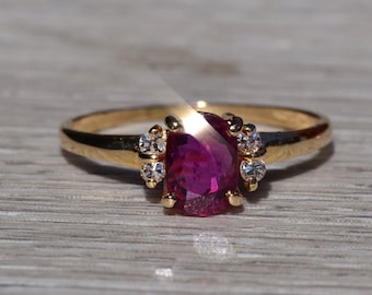 May include: A gold ring with a large oval-shaped ruby gemstone surrounded by smaller clear gemstones.