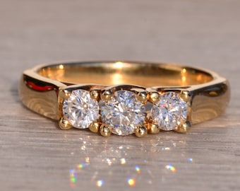 May include: A gold band ring with three round diamonds set in prongs. The diamonds are clear and sparkly.
