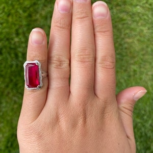 May include: A silver ring featuring a large, rectangular, red gemstone set in a filigree design.