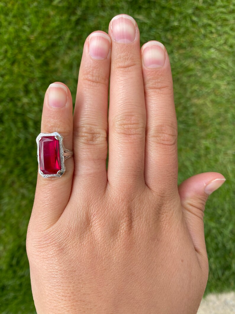 May include: A silver ring featuring a large, rectangular, red gemstone set in a filigree design.