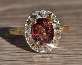 May include: A gold ring with a large oval-shaped red gemstone surrounded by a halo of smaller white gemstones.