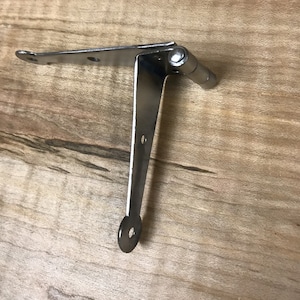 May include: A silver metal hinge with a rounded end. The hinge is folded at a 90-degree angle.