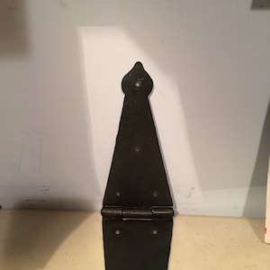 Puede incluir: Una bisagra de correa decorativa negra con una parte superior puntiaguda y una articulación con bisagras. La bisagra es de metal y tiene varios orificios para tornillos para el montaje. Ideal para puertas o portones.