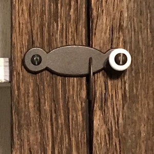 May include: A black metal latch with a white knob, mounted on a wooden door.