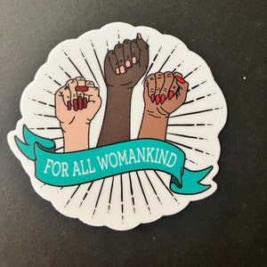 Può includere: Un adesivo bianco con tre pugni alzati in diverse tonalità di pelle, ognuno con lo smalto rosso. I pugni sono circondati da un design a raggiera e uno stendardo turchese con il testo "FOR ALL WOMANKIND".