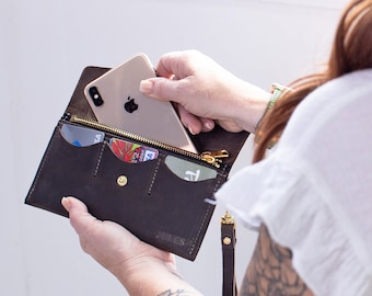 May include: A brown leather wallet with a zipper closure and multiple card slots. A gold smartphone is being placed into the wallet.