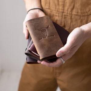 May include: A stack of three leather notebooks with a brown, burgundy, and black color scheme. The top notebook has a bull's head design and the text "Oak Tan Leather" embossed on the front cover.