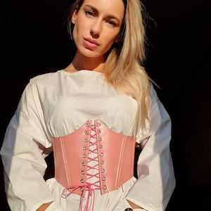May include: A pink leather corset belt with a lace-up front. The belt is tied in a bow at the front and has silver eyelets.