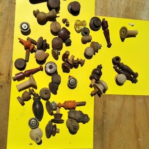 Könnte beinhalten: Eine Sammlung von antiken Holz- und Metall-Schubladenknöpfen und -griffen in verschiedenen Formen, Größen und Farben. Die Knöpfe sind auf einer gelben Oberfläche angeordnet.