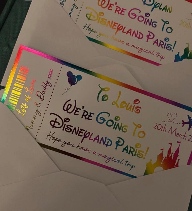 K&ouml;nnte beinhalten: Zwei Disneyland Paris-Tickets in wei&szlig;en Umschl&auml;gen. Die Tickets zeigen einen Regenbogen-Text mit der Aufschrift "We're Going To Disneyland Paris!" und "Hope you have a magical trip." Ein Ticket ist an "To Louis" adressiert.