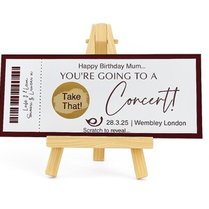 Könnte beinhalten: Ein Geburtstags-Konzertticket mit einem weinroten Rand, präsentiert auf einer kleinen Holzstaffelei. Auf dem Ticket steht "Happy Birthday Mum... YOU'RE GOING TO A Concert!" mit einem Rubbelfeld und dem Datum 28.3.25 in Wembley London.