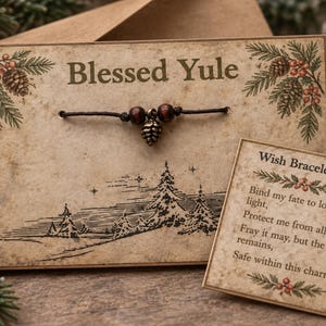 May include: A brown cord bracelet with two dark wooden beads and a small metallic pinecone charm, mounted on a tan card printed with the text Blessed Yule, pine branch illustrations, and a separate square card with the Wish Bracelet Spell text.