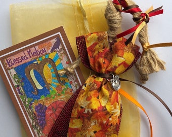 May include: A small, handmade doll dressed in a fabric with a fall leaf pattern. The doll has brown hair and is wearing a silver charm. The doll is packaged in a yellow organza bag with a card that says "Blessed Mabon".