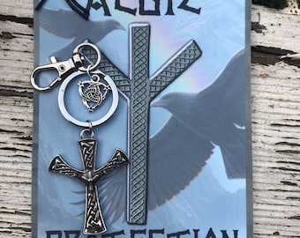 May include: A silver key chain with a silver cross charm and a silver knot charm. The keychain is hanging from a sign with the word "ALGIZ" and the word "PROTECTION" printed on it.