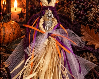 May include: A handcrafted straw doll figure featuring a braided loop head, adorned with purple yarn, orange and purple ribbons, and white tulle fabric. The doll includes silver-toned metal charms shaped like a ship wheel and a crescent moon.