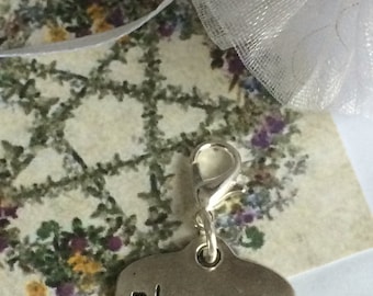 May include: Silver charm with a heart-shaped tag that says "Blessings" on a white background with a floral design.