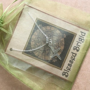 May include: A silver necklace with a Celtic cross pendant on a green organza bag with a card that reads "Blessed Brigid".