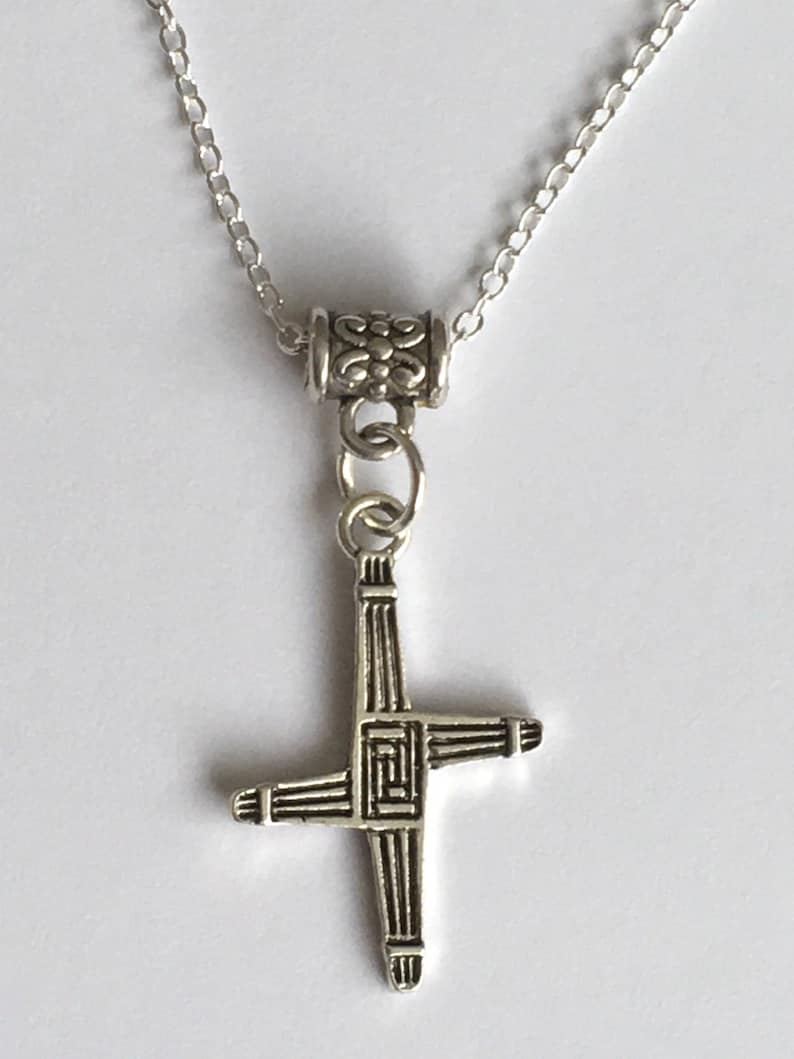 May include: A silver chain necklace with a silver Celtic cross pendant. The cross is detailed with intricate designs.
