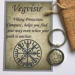 Könnte beinhalten: Ein silberner Schlüsselanhänger mit einem runden Anhänger mit dem Vegvisir-Symbol, einem Wikinger-Kompass-Design. Der Anhänger befindet sich neben einer Karte mit dem Text "Vegvisir Viking Protection Compass, helps you find your way even when your path is unclear."