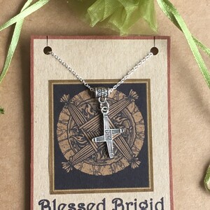 May include: Silver necklace with a Celtic cross pendant on a brown card with the text "Blessed Brigid".