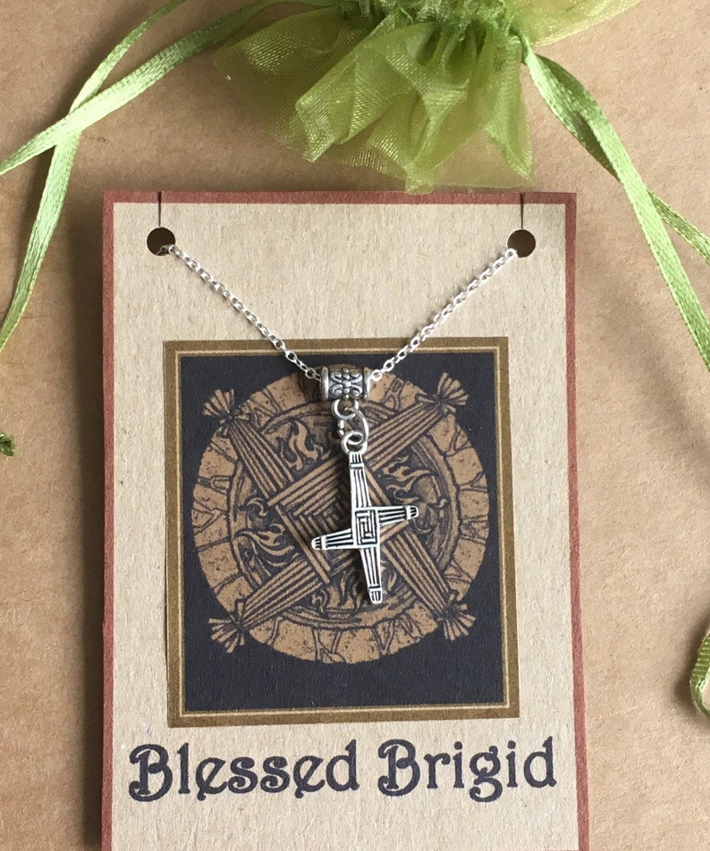 May include: Silver necklace with a Celtic cross pendant on a brown card with the text "Blessed Brigid".