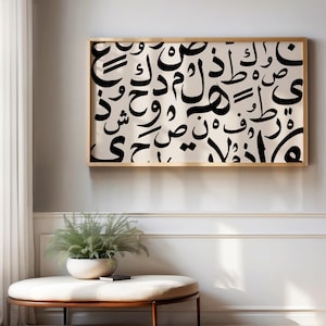 以下が含まれることがあります： 金色の額縁に入ったアラビア語の書道の白黒プリント。プリントはクリーム色の背景に、さまざまな文字や記号が描かれています。