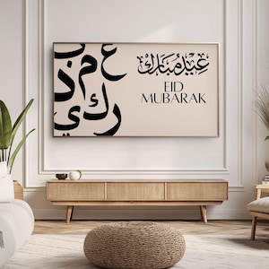 May include: A beige wall with a framed print featuring black Arabic calligraphy that reads "Eid Mubarak". The print is hanging above a light wood media console with a woven rattan front. A woven brown ottoman sits in front of the console. A beige rug with a white geometric pattern is on the floor.