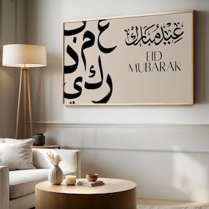 May include: A rectangular wall art piece in a light beige frame featuring black Arabic calligraphy on the left side and the black text "EID MUBARAK" in both Arabic script and English capital letters on the right side against a beige background.