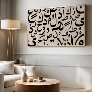 May include: A rectangular wall art piece featuring black Arabic calligraphy characters printed on a light beige background, enclosed within a thin wooden frame. The composition displays a dense arrangement of various script letters.