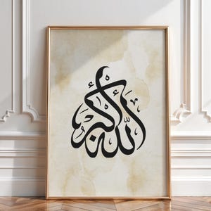May include: Framed artwork featuring black Arabic calligraphy on a beige watercolor background. The calligraphy is the central focus, presented in an elegant, flowing script. The artwork is encased in a gold-colored frame, adding a touch of sophistication to the piece.